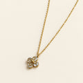 A delicate gold chain necklace with a small four-petal flower pendant, resting on a soft beige textured surface.
